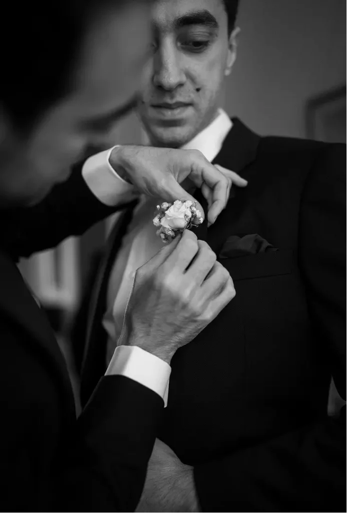 Un proche aide le marié à fixer sa boutonnière rose et gypsophile